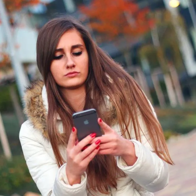 Une jeune femme lit un message sur son téléphone, en ville